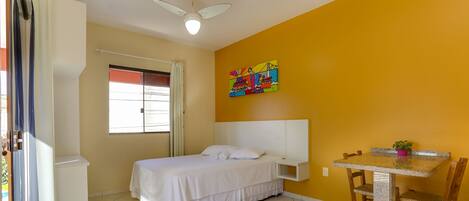 A room with a bed, a small table, and a ceiling fan.