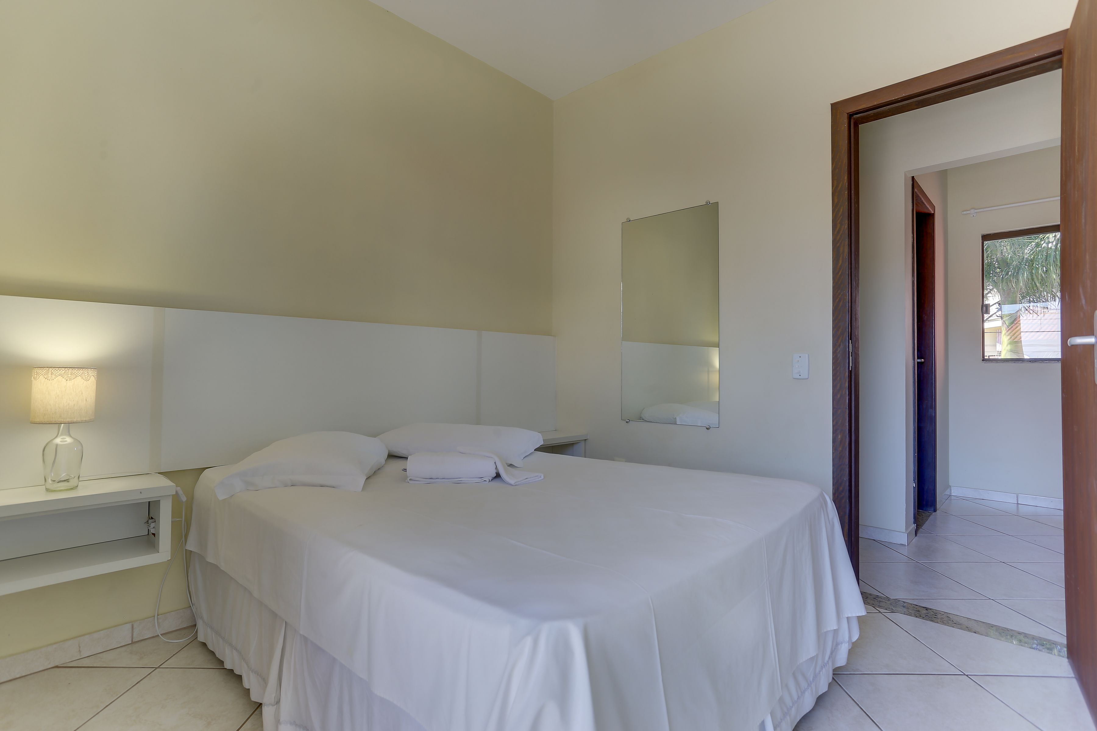 Un dormitorio con cama, mesita de noche, lámpara y espejo en la pared.