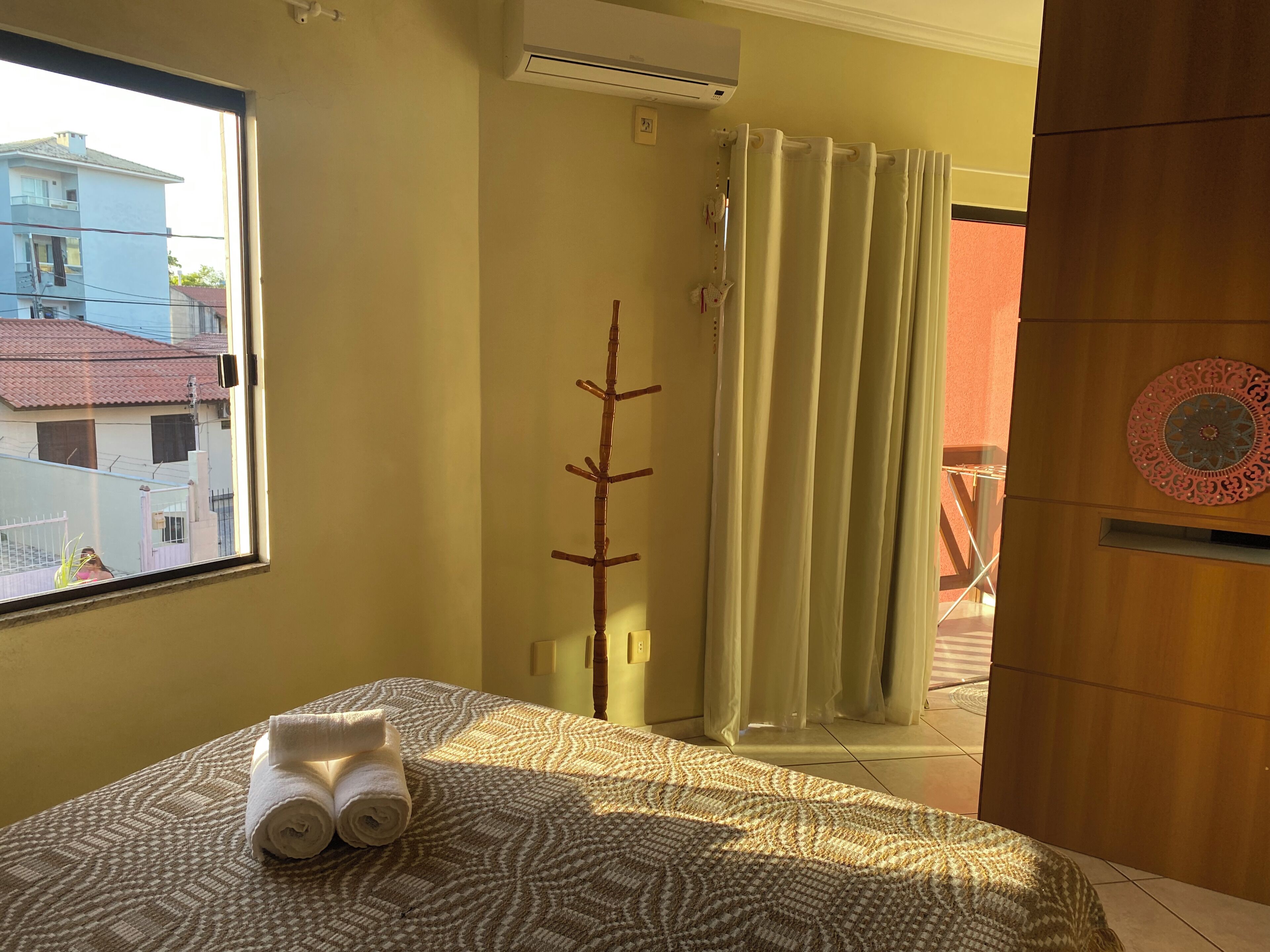 Una camera d'albergo con un letto, una finestra, un condizionatore d'aria, una tenda e vista sugli edifici esterni.