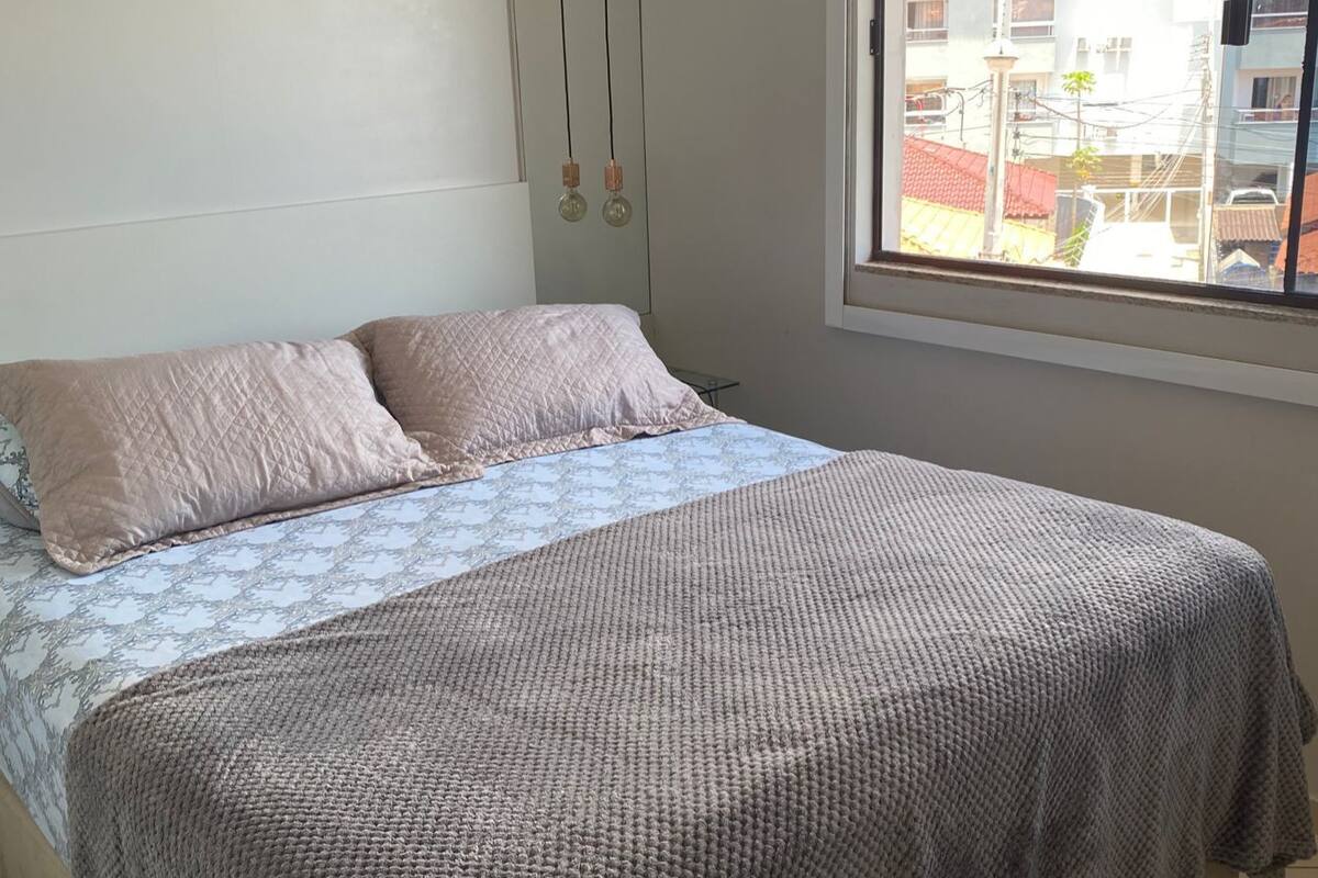 A bedroom with a bed, a window, and a view of buildings outside.