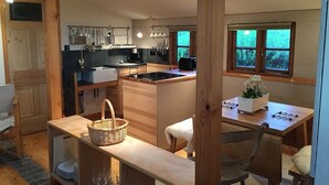 Eine moderne Küche mit Holzelementen, ein Essbereich mit Tisch und Stühlen sowie große Fenster mit Blick ins Freie.