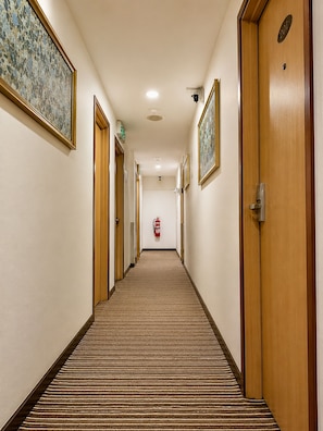 Un pasillo de hotel con puertas de madera, obras de arte enmarcadas, un extintor y suelo alfombrado.