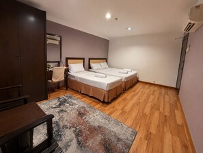 A hotel room with two beds, a desk, a chair, a coffee maker, and an air conditioning unit. - Royal Queenspark Hotel (Malacca City)