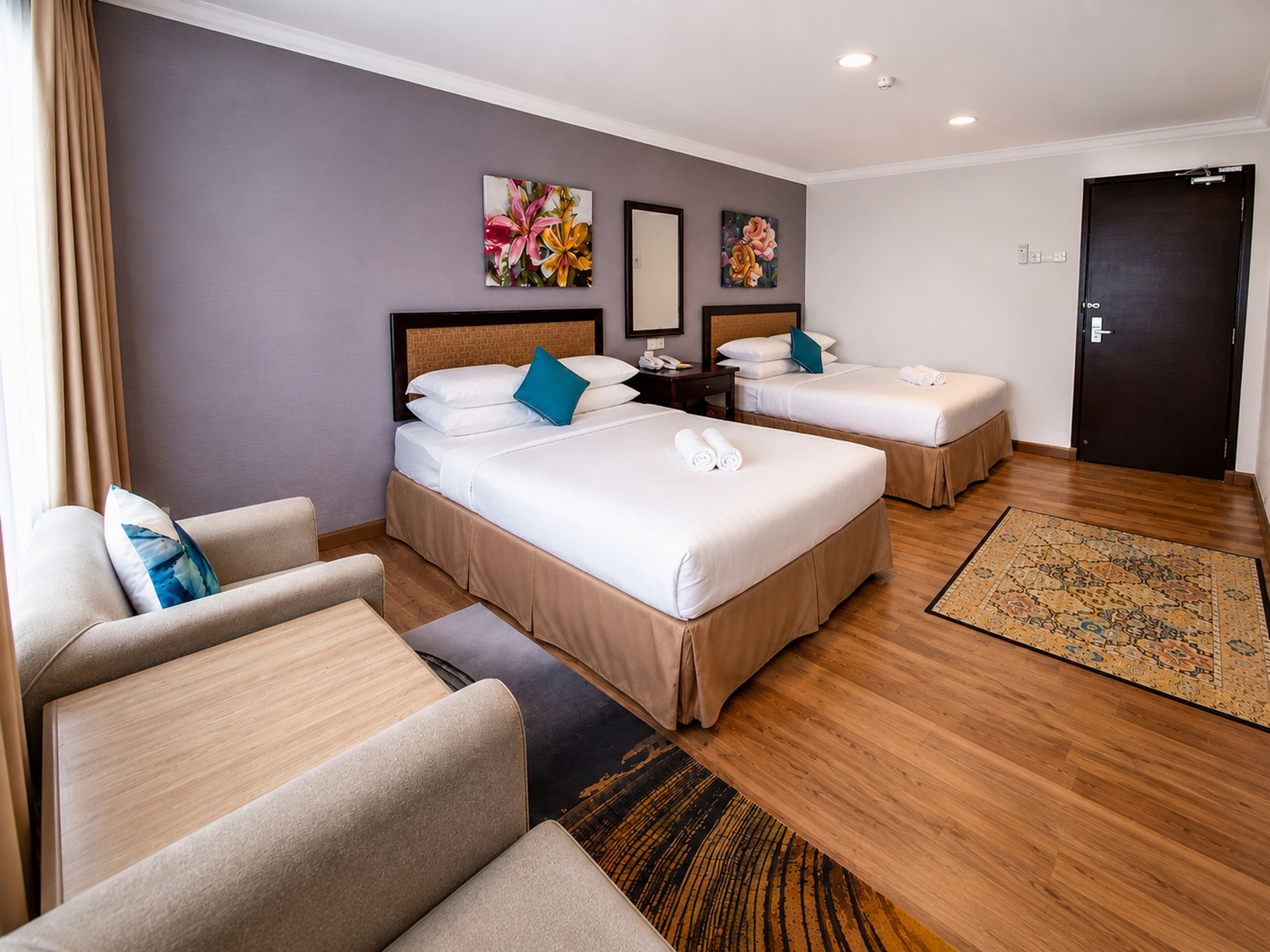 A hotel room with two beds, a sofa, a desk, and a door.