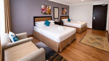 A hotel room with two beds, a sofa, a desk, and a door.