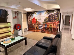 Un vestíbulo de hotel con un mural grande, una recepción, un área de descanso y un pasillo.