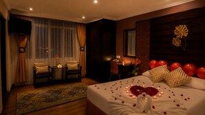 A hotel room with a bed, a desk, a chair, a small table with a lamp, and a window with curtains. - Royal Queenspark Hotel (Malacca City)