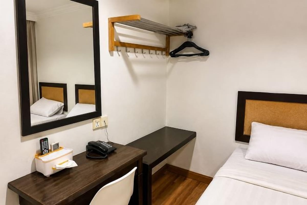 A hotel room with a bed, a desk with a mirror, a telephone, and a hanging clothes rack.
