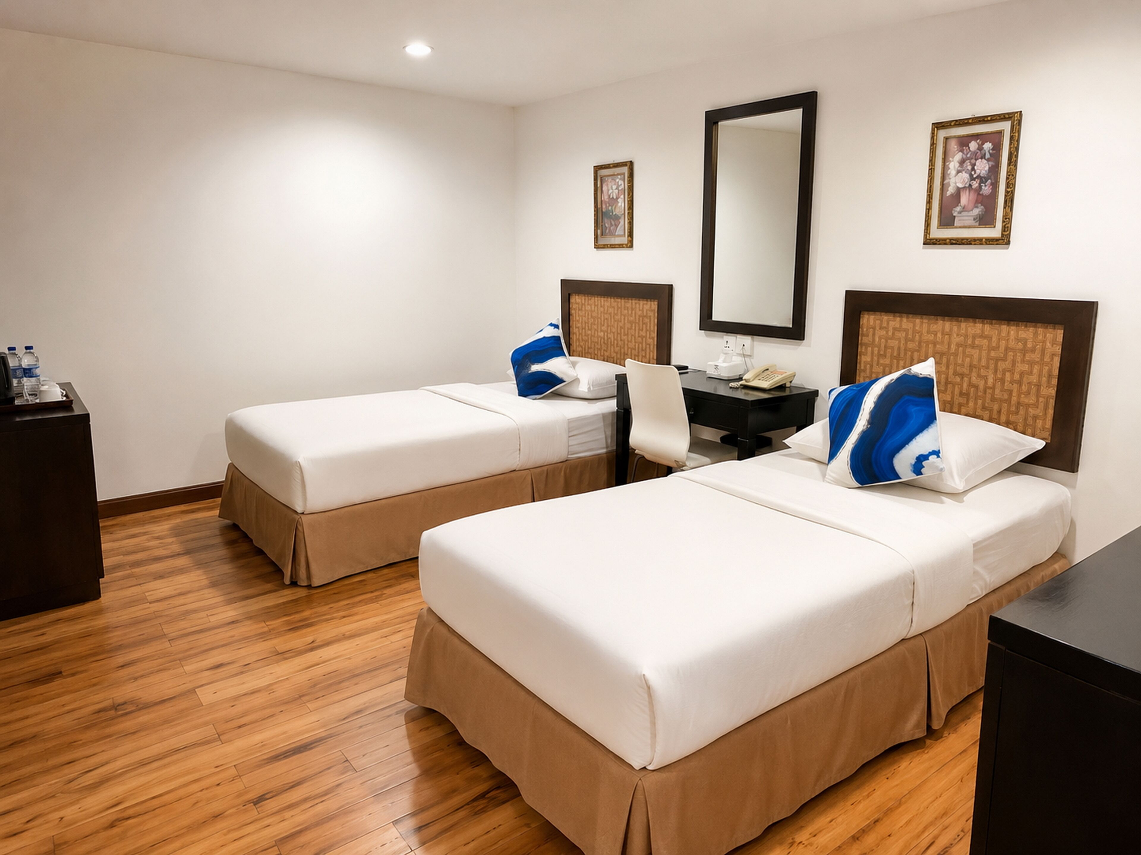A hotel room with two single beds, a desk, a chair, a dresser, and a mirror.
