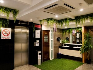 A modern bathroom with a no-smoking sign, an elevator, a mirror, and artificial greenery. - Royal Queenspark Hotel (Malacca City)