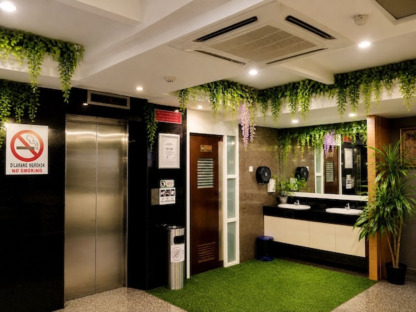 A modern bathroom with a no-smoking sign, an elevator, a mirror, and artificial greenery. - Royal Queenspark Hotel (Malacca City)