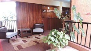 A reception area with a wooden wall, a reception desk, a sofa, a coffee table, and a large potted plant. - Sky Hotel Nairobi (Nairobi)