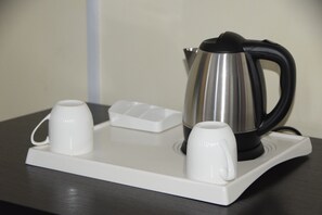 Una tetera de acero inoxidable con asa negra sobre una bandeja blanca con dos tazas blancas.