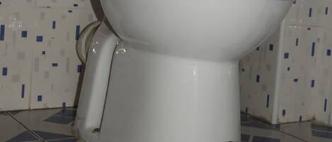 A white toilet with a closed lid, positioned against a tiled wall with a blue and white pattern.