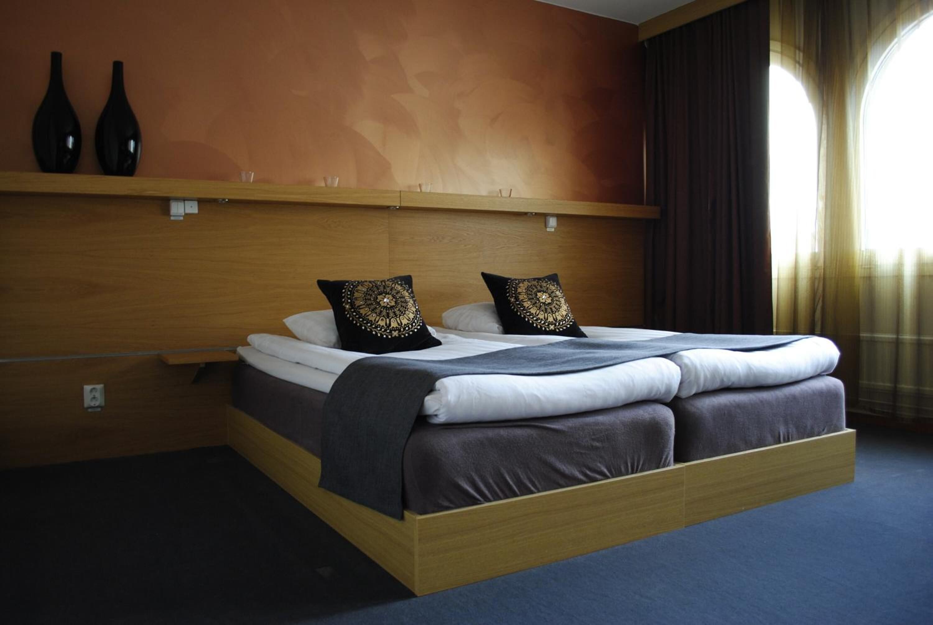 Un letto ben rifatto con una testiera in legno, due cuscini decorativi e un comodino con vasi.