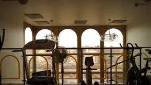 Un gimnasio con equipo de ejercicio, ventanas amplias y vistas de la ciudad.
