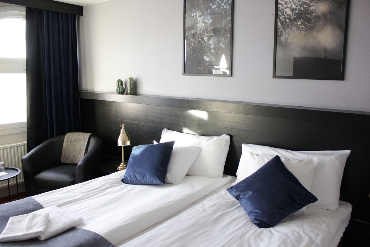 Habitación de hotel con cama, dos sillas, una mesita y una obra de arte en la pared.