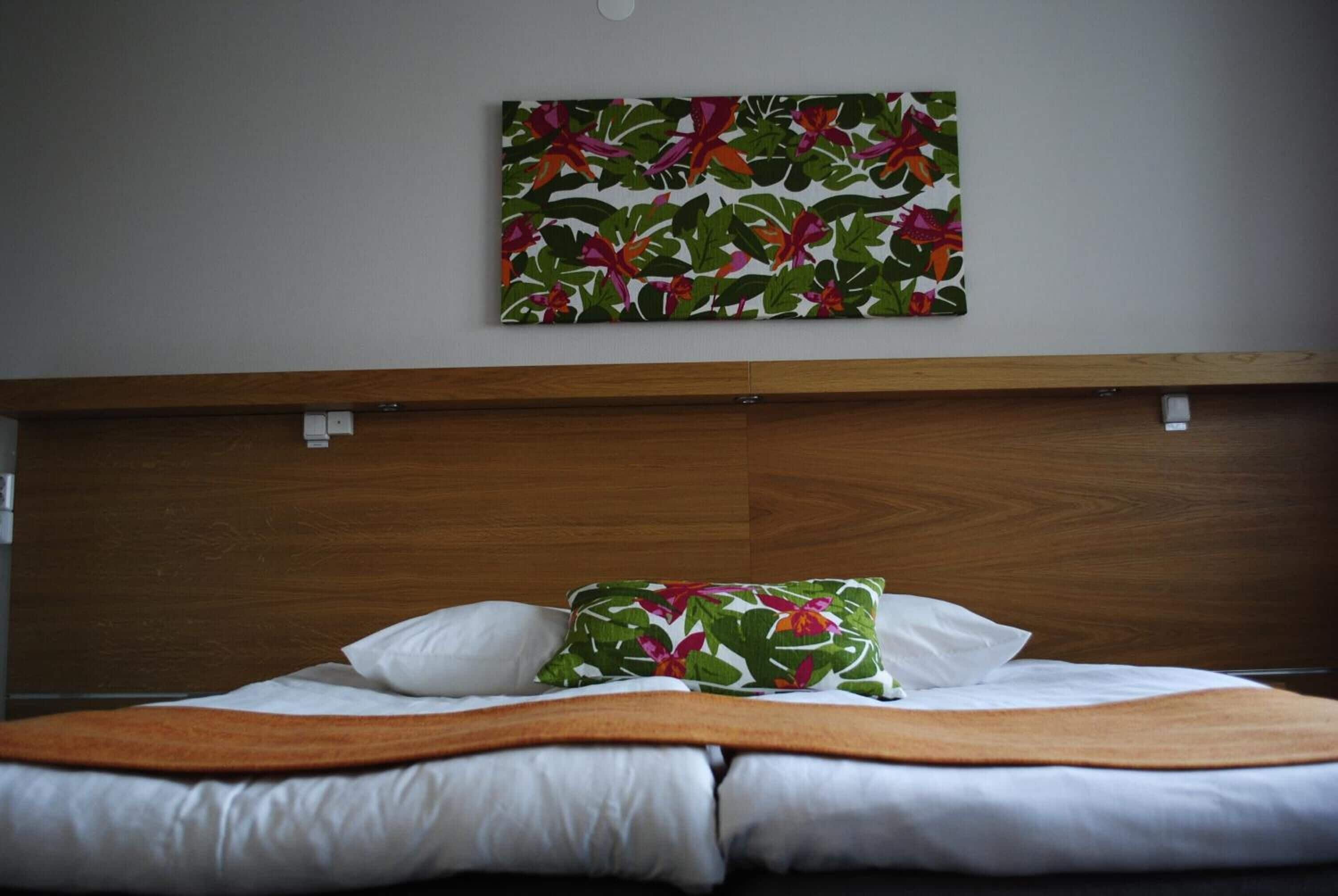 A hotel room with a wooden headboard, a bed with white linens, and a floral-patterned pillow.