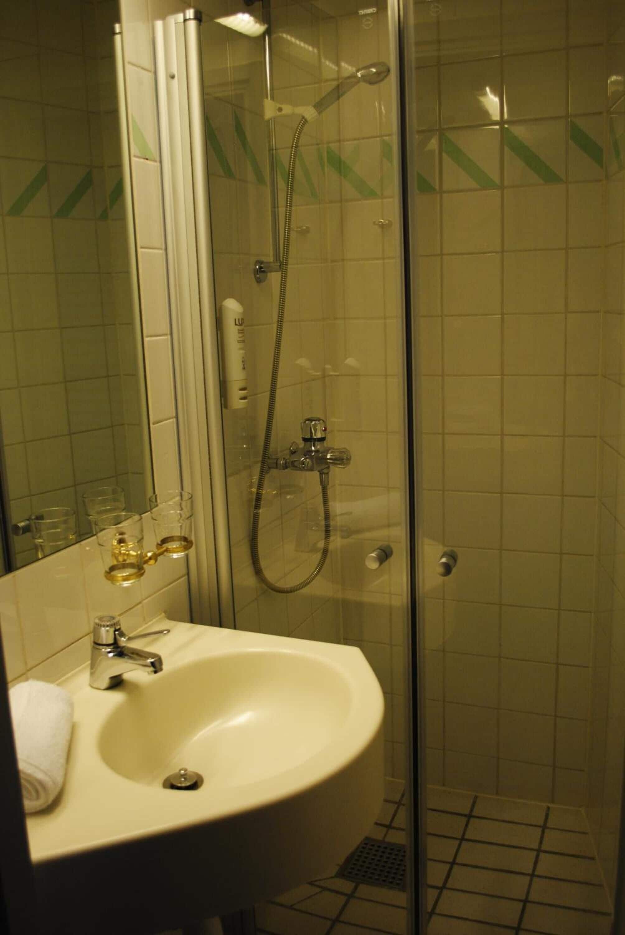 Un baño con ducha de vidrio, lavamanos con espejo y paredes de azulejos.