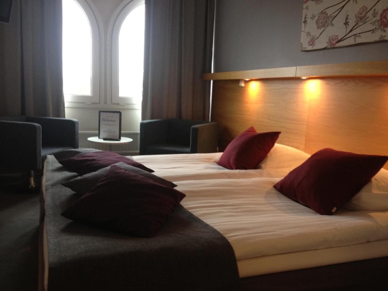A hotel room with a large bed, two red pillows, a small table, and two chairs.