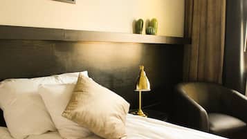Camera d'albergo con un letto, una scrivania con lampada, una sedia e una mensola a parete con oggetti decorativi.