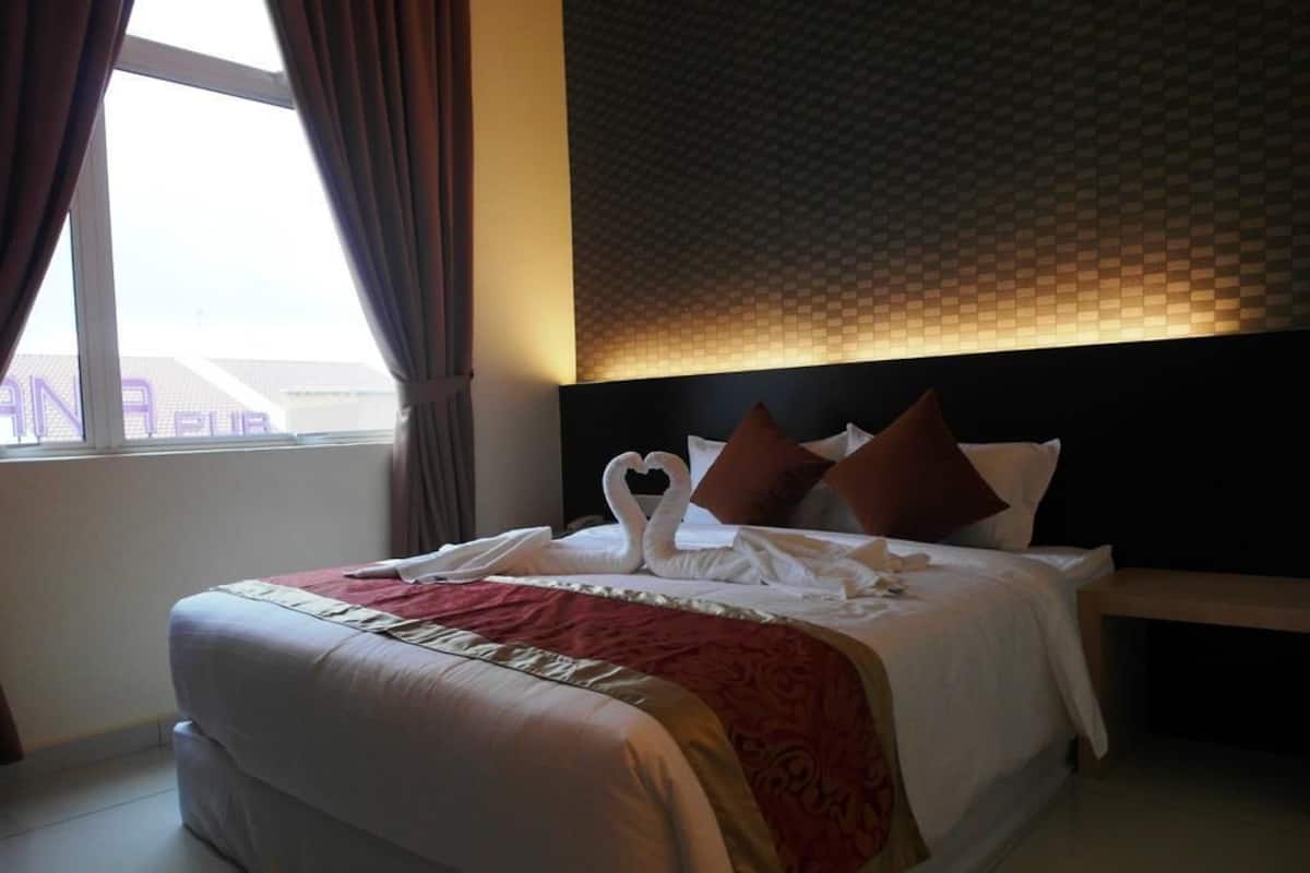 A neatly made bed with a red and white bedspread, a wooden headboard, and a window with curtains.