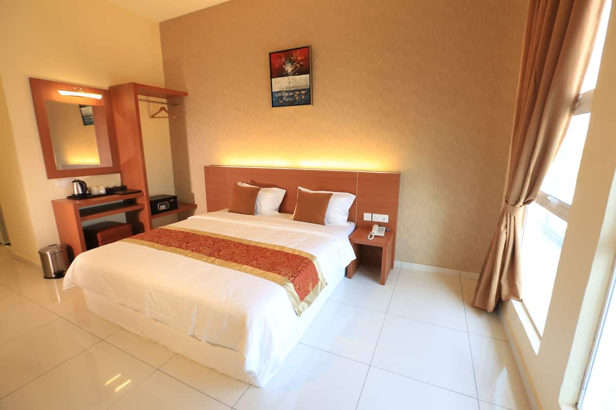 A hotel room with a large bed, a bedside table, a mirror, a small desk, and a window with curtains.