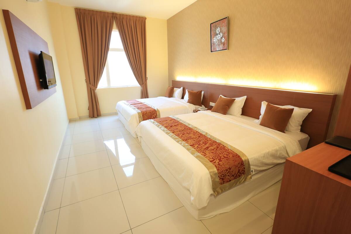 A hotel room with two beds, a flat-screen TV mounted on the wall, a window with curtains, and a framed picture on the wall.