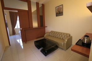 A modern living room with a leather sofa, a glass coffee table, and a kitchen area with a kettle.