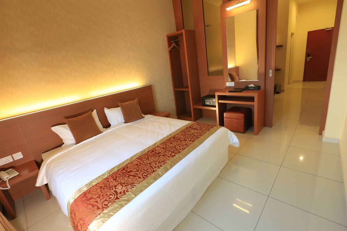 A hotel room with a large bed, a bedside table with a phone, a desk with a chair, and a mirror.