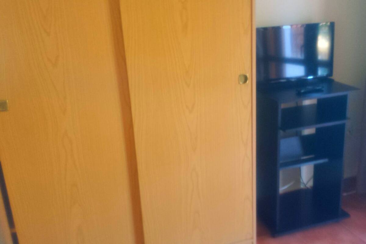 Una habitació amb una porta de fusta, un moble de televisió negre amb un televisor de pantalla plana i una cortina a la finestra.
