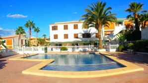A pool area with a white fence, palm trees, and a building with multiple windows and balconies. - Hostal Bahía Blanca (Alicante)