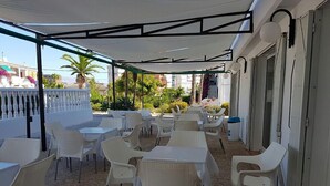 An outdoor patio area with white plastic tables and chairs, covered by a white canopy. - Hostal Bahía Blanca (Alicante)