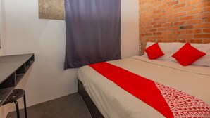 Een slaapkamer met een bakstenen muur, een bed met rode kussens, een bureau en een stoel.