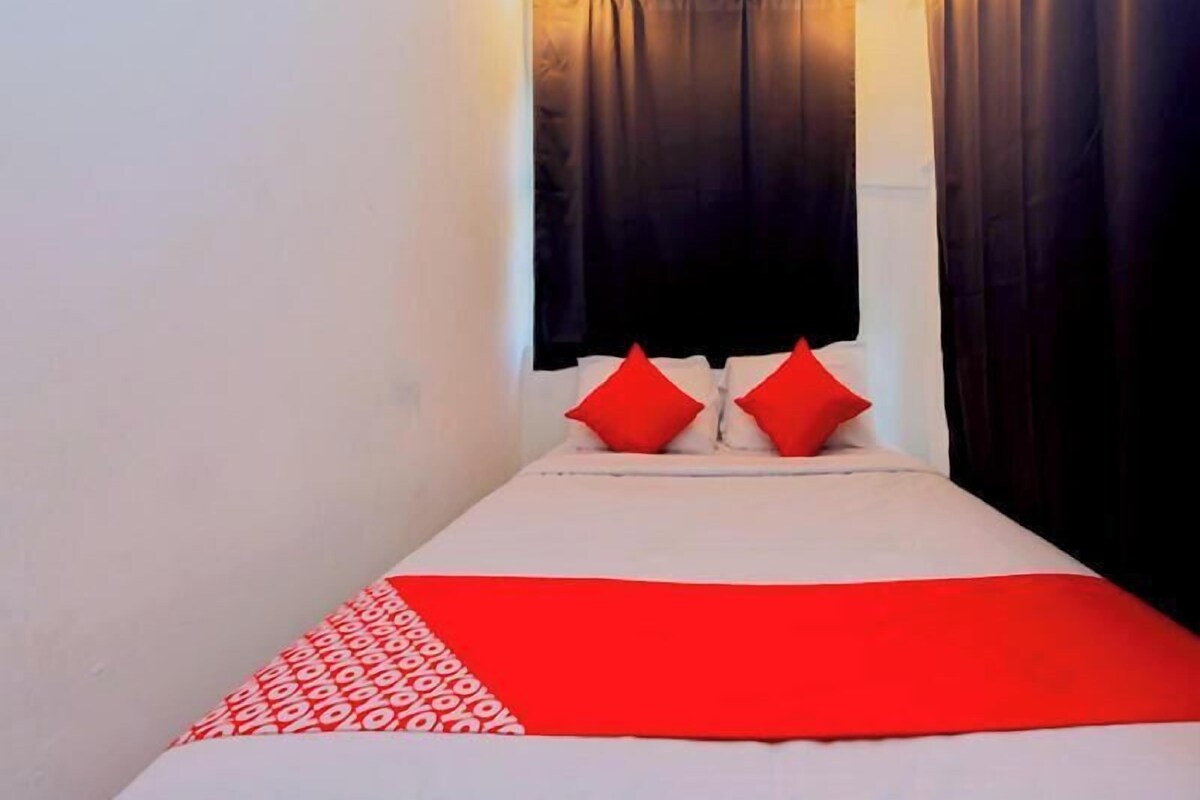 Una cama con una colcha blanca y roja, dos almohadas rojas y una cortina negra.