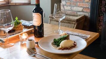 A dining table with a bottle of wine, two glasses, a plate with food, and a candle.