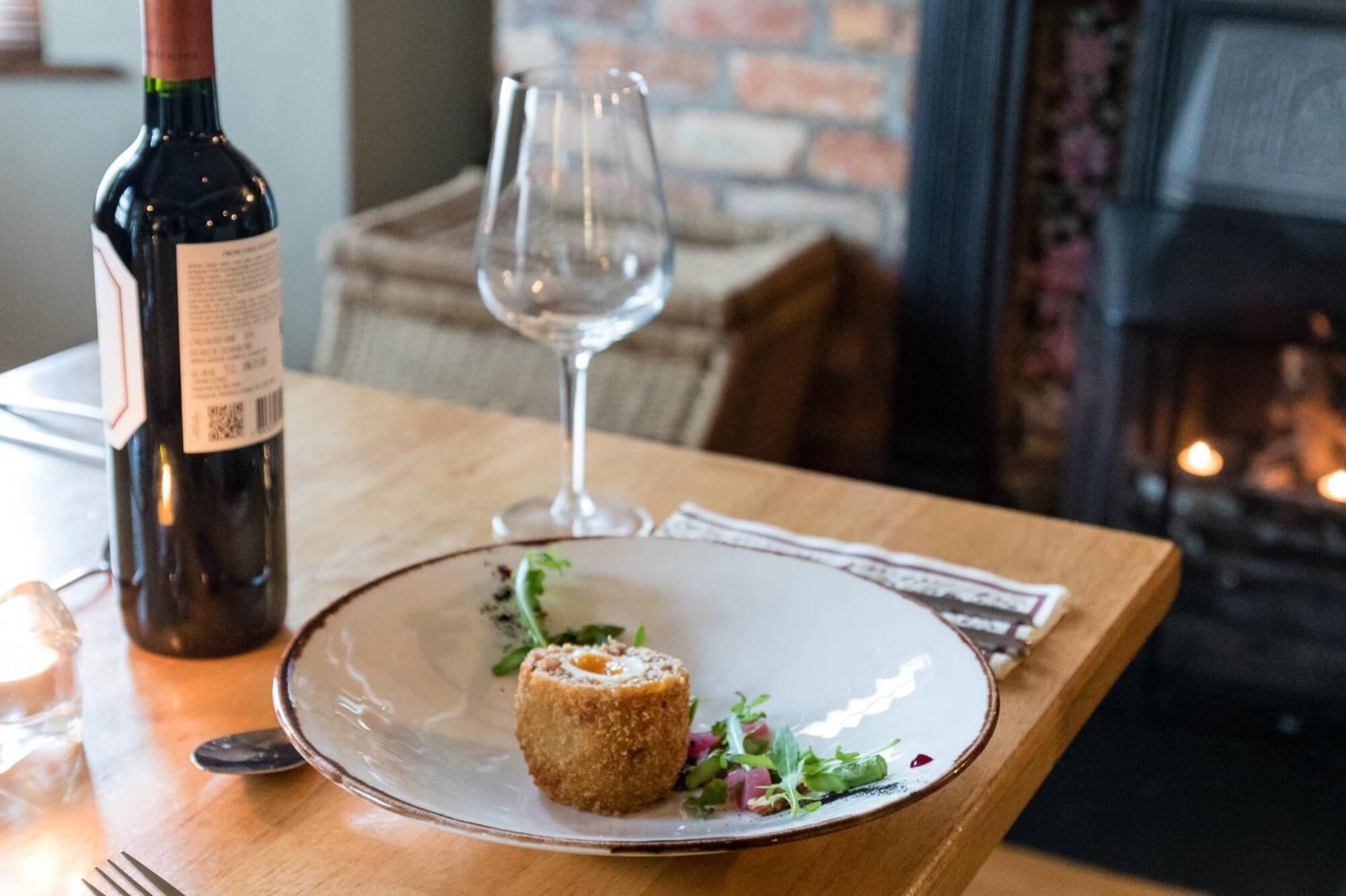 Une table avec une bouteille de vin, un verre et une assiette contenant un plat.
