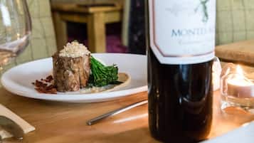 A plate with a meat dish and broccoli, a bottle of wine, and a candle on a wooden table.