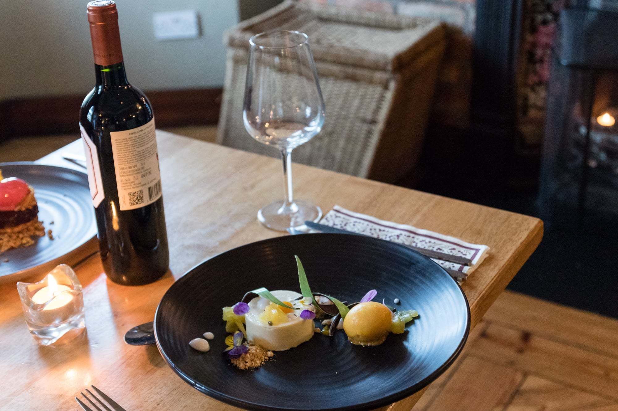 Een eettafel met een fles wijn, een wijnglas en een bord eten.
