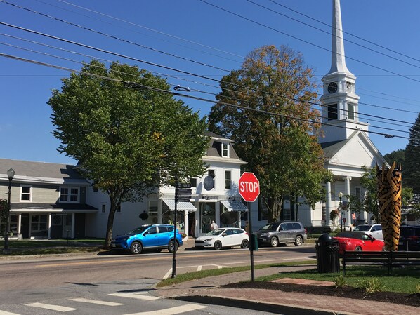 A street view with a stop sign, a church with a steeple, and parked cars. - 109 Main Street (Stowe)