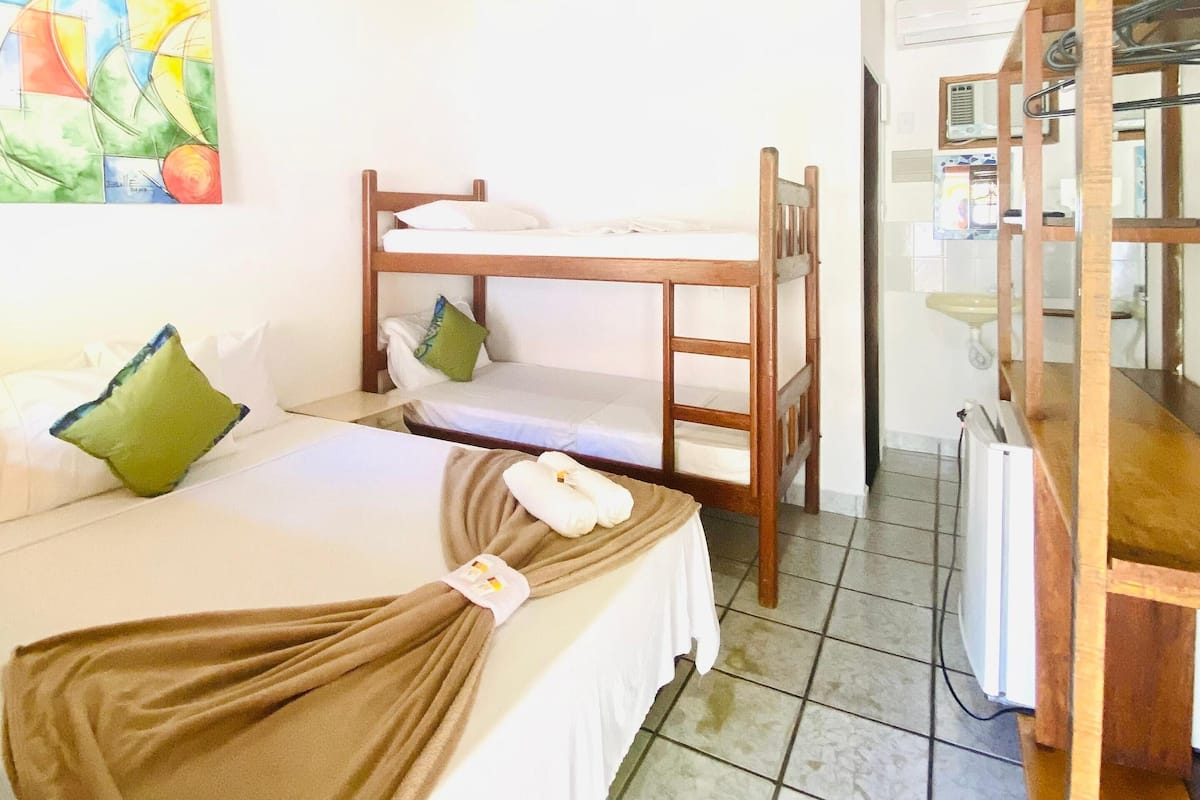 Una habitación con literas, una cama individual, un ventilador de techo, un cuadro y una pequeña cocina.