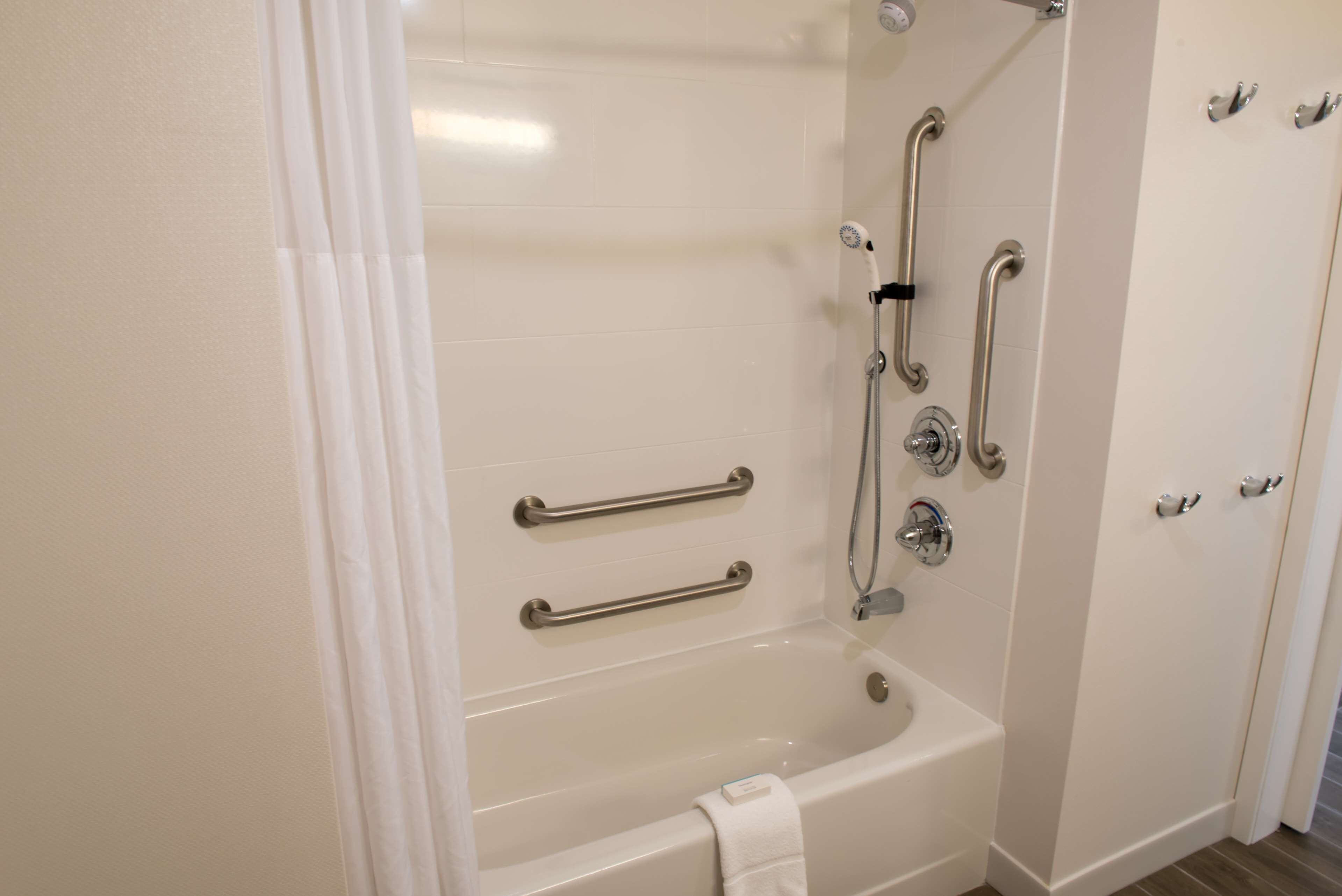 A modern bathroom with a bathtub, grab bars, and a shower head.
