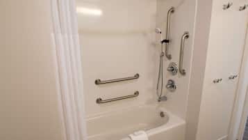A modern bathroom with a bathtub, grab bars, and a shower head.
