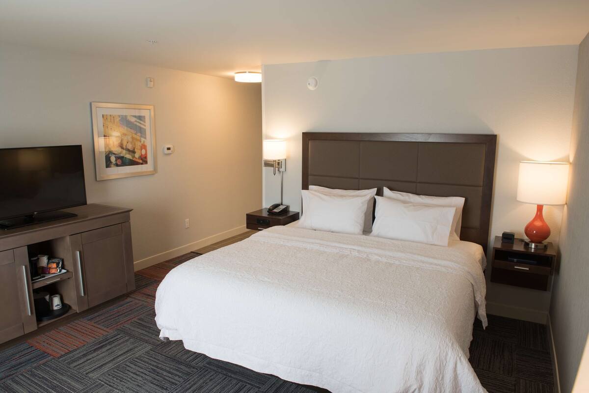 A hotel room with a large bed, a TV, a desk, and a nightstand with a lamp.
