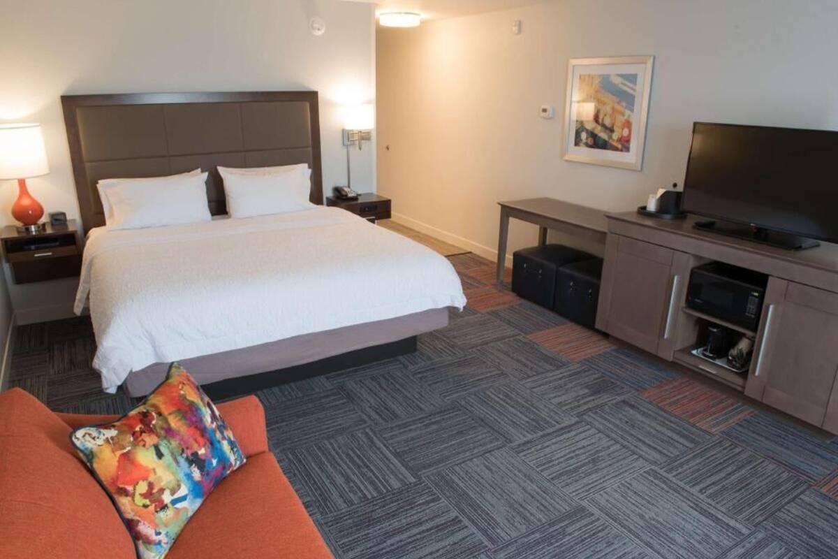 A hotel room with a large bed, a television, a desk, and a sofa.