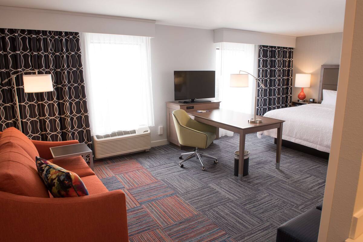 A hotel room with a bed, a desk with a TV, a couch, and a patterned carpet.