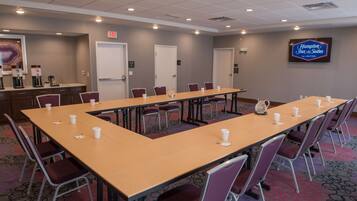 A conference room with a long table, chairs, a coffee station, and a Hampton Inn sign.
