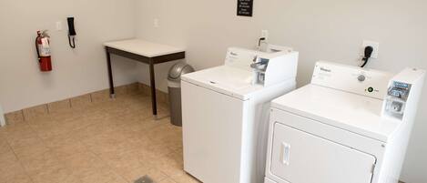 A laundry room with two Whirlpool washers, a table, a trash can, and a fire extinguisher.
