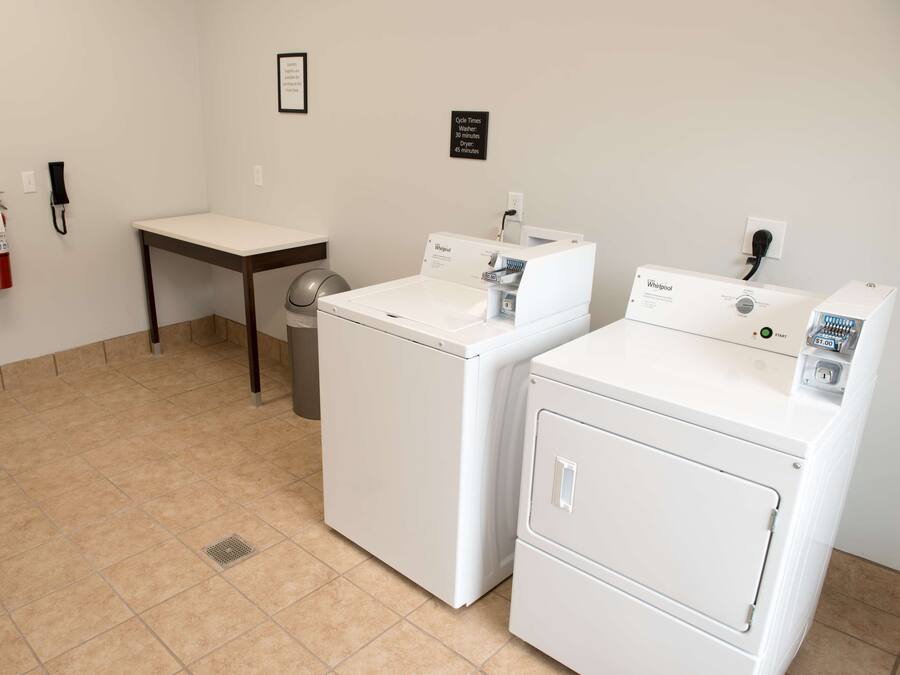 Un lavadero con dos lavadoras Whirlpool, una mesa, un bote de basura y un extintor.