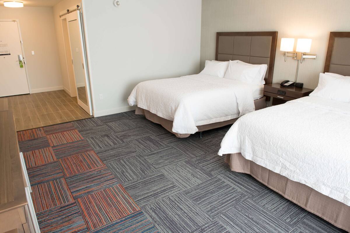 A hotel room with two beds, a nightstand with a lamp, and a carpeted floor.